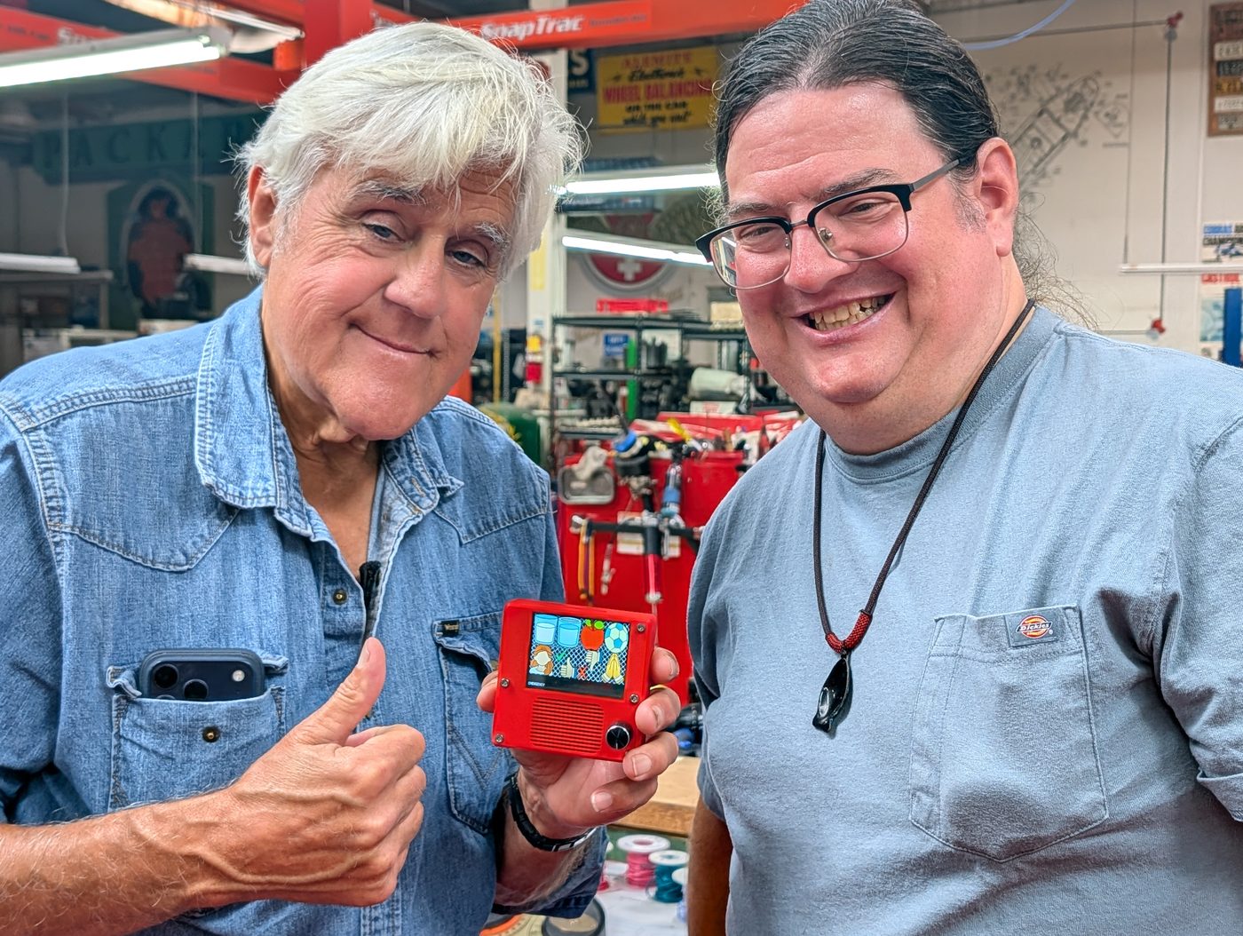Jay Leno smiling and holding a red T-Rex Talker device next to T-Rex
