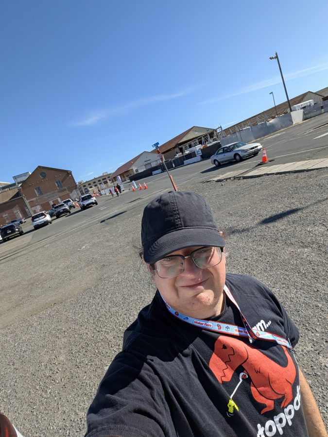T-Rex on Mare Island in a black cap and R.O.A.R. T-shirt, Maker Faire lanyard on