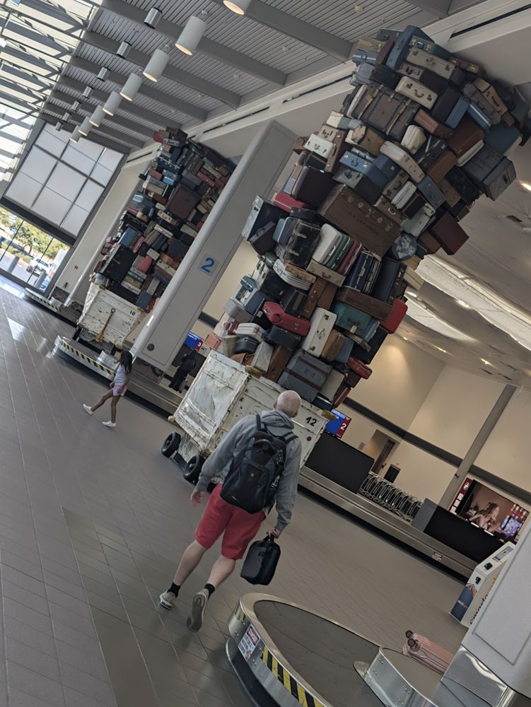 Airport baggage claim with a tall sculpture of stacked vintage suitcases