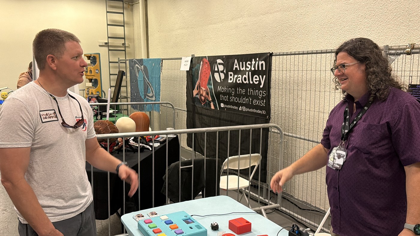 Destin Sandlin from Smarter Every Day chatting with T-Rex at the R.O.A.R. Open Sauce booth, with the T-Rex Talker button board on the table between them